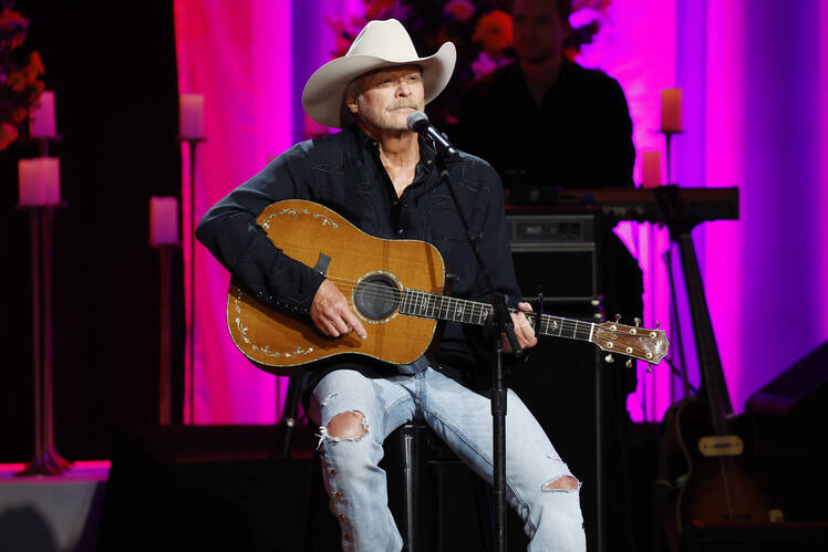 Alan Jackson sits on stage with his guitar