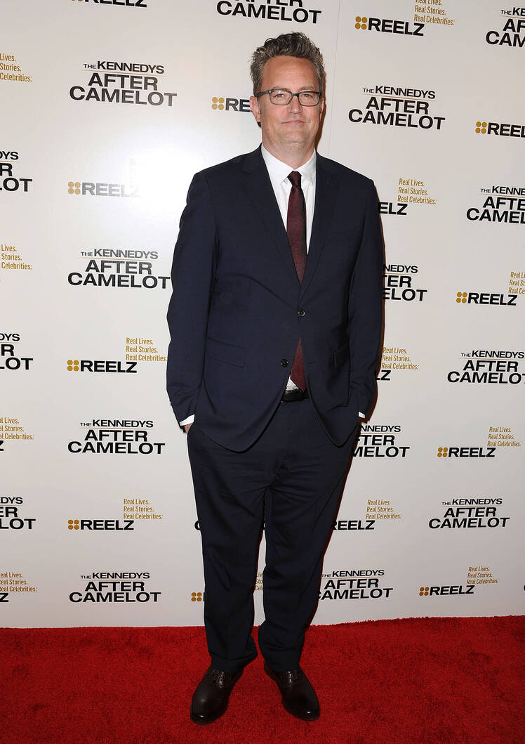 Matthew Perry stands with his hands in his pockets in a suit