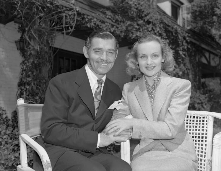 Carole Lombard and Clark Gable smile while sitting next to each other