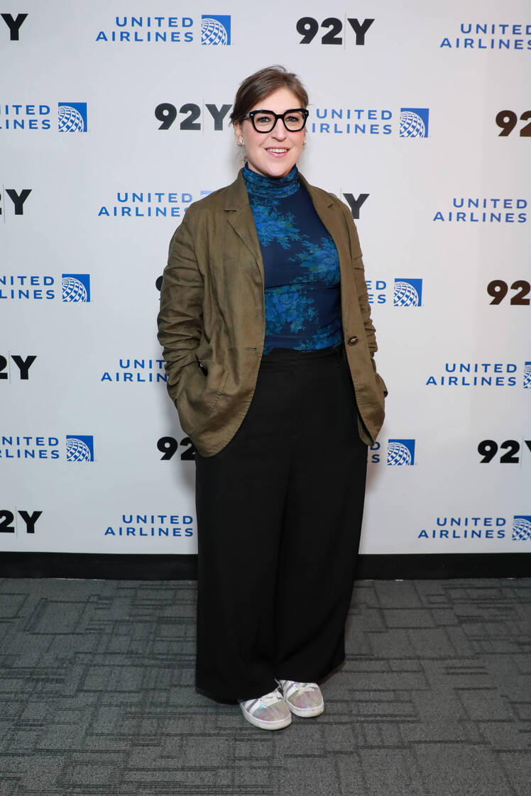 Mayim Bialik wears a blue top with black pants and a green jacket